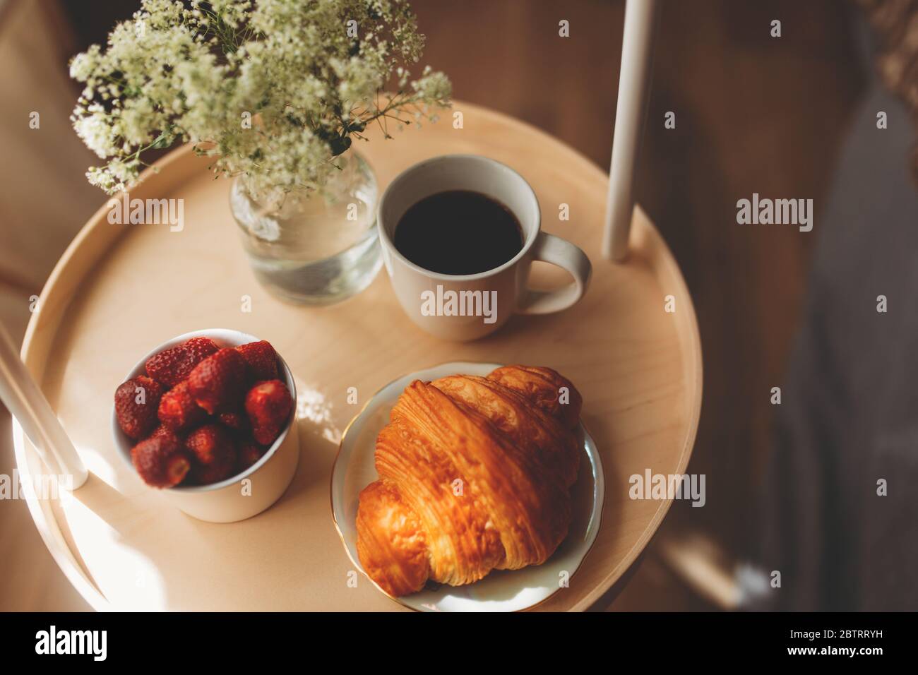 Desayuno en una bandeja en la cama en casa ropa blanca oscura. Croissant té fresas. Foto de stock