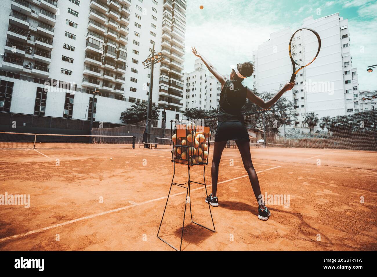Vista gran angular desde detrás de una joven mujer biroquial delgada apuntando un golpe antes de golpear una pelota de tenis durante un entrenamiento deportivo o calentamiento en un exterior Foto de stock