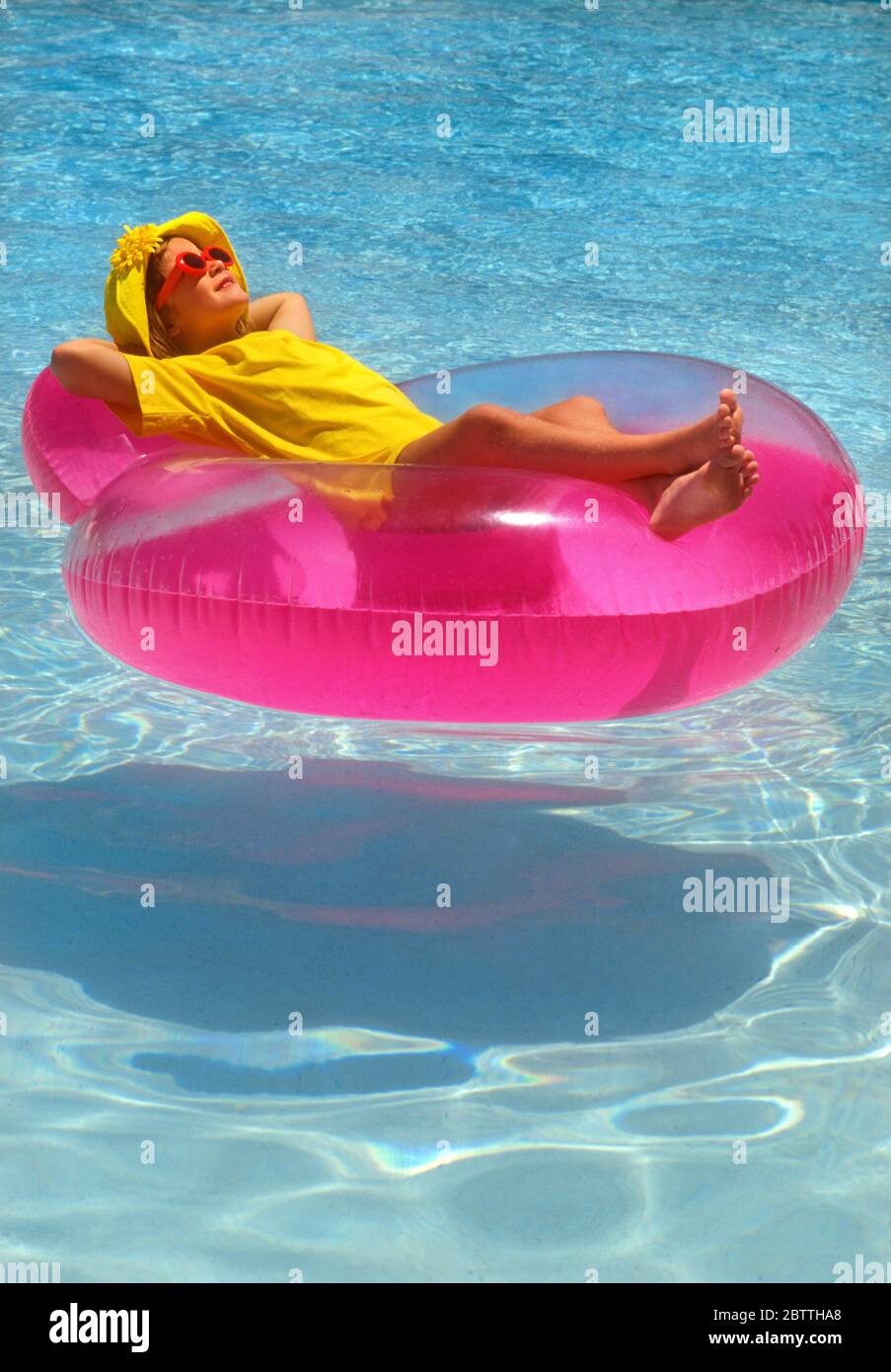 chica 5-6 años piscina en lilo rosa flotador en vacaciones usando sol seguro camiseta sombrero y gafas de sol relajante y. relajarse en la piscina junior Foto de stock