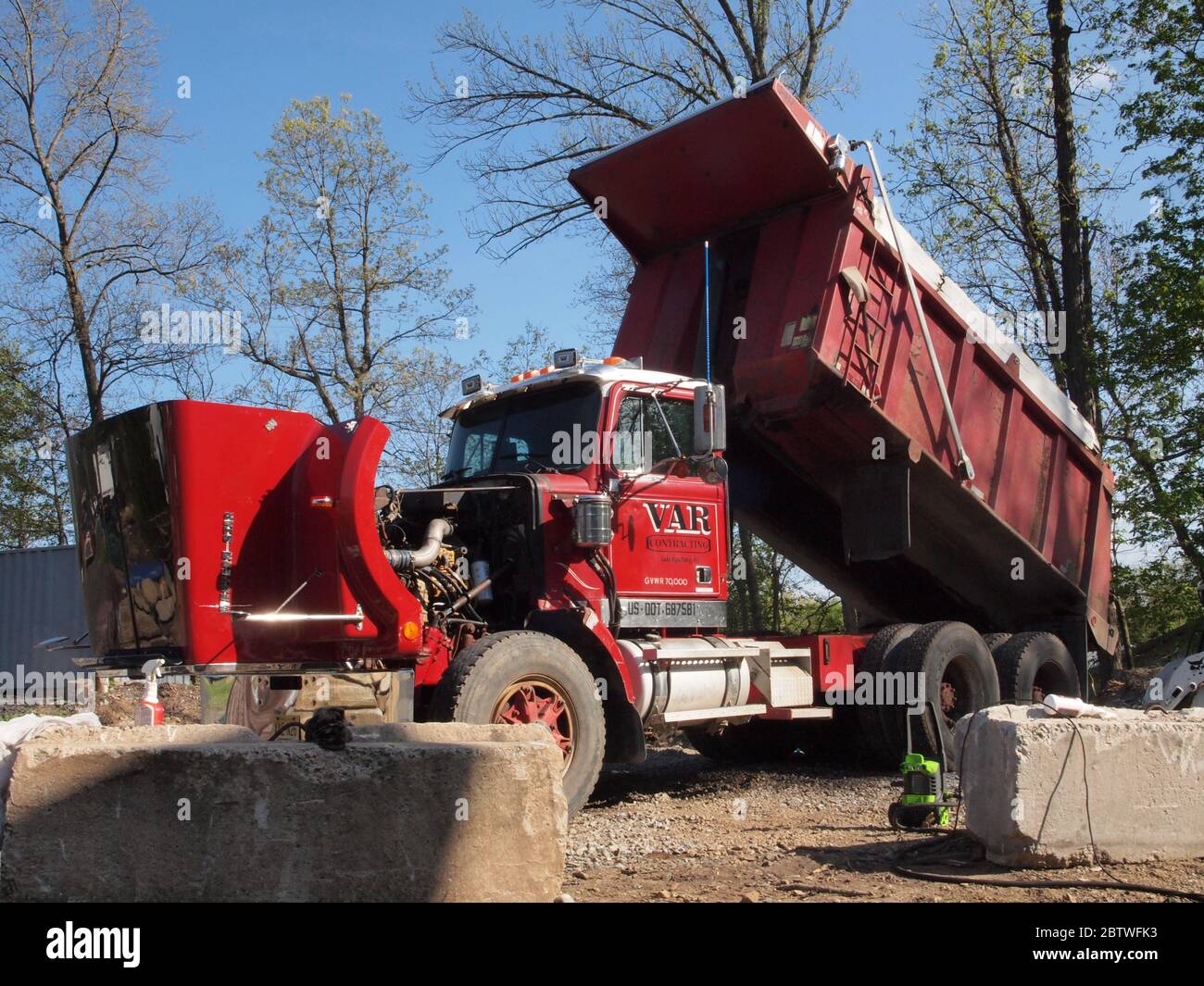 Dúmper de servicio pesado antiguo con su capó abierto para trabajos mecánicos. Camión volquete típico de América del Norte grande ubicado en un patio de contratistas. Foto de stock