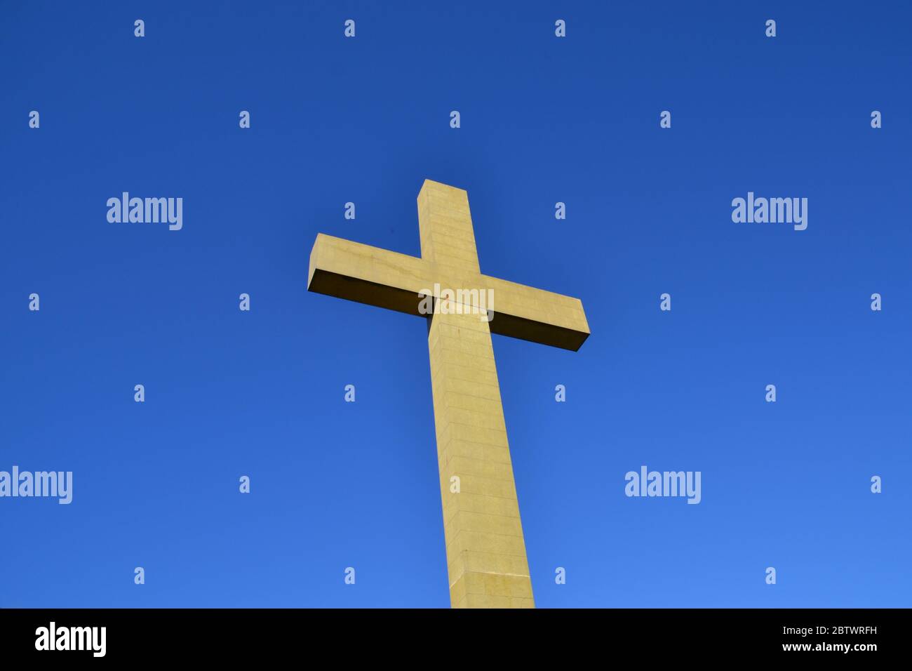 Vista de ángulo bajo de una cruz religiosa cristiana concreta contra un cielo azul cobalto claro Foto de stock