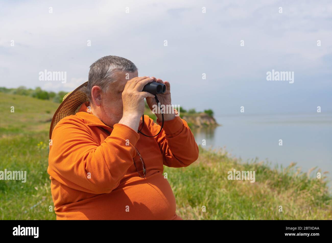 Retrato al aire libre de un hombre mayor mirando binocular mientras se sienta en la ribera de Dnipro en la temporada de primavera Foto de stock