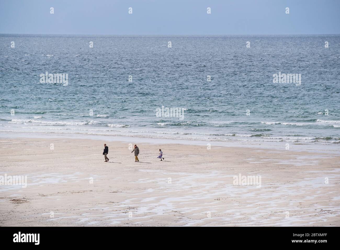 Debido a la pandemia de Coronavirus Covid 19, la playa Fistral, normalmente ocupada, está vacía, excepto para tres personas caminando por la costa en Newquay i. Foto de stock