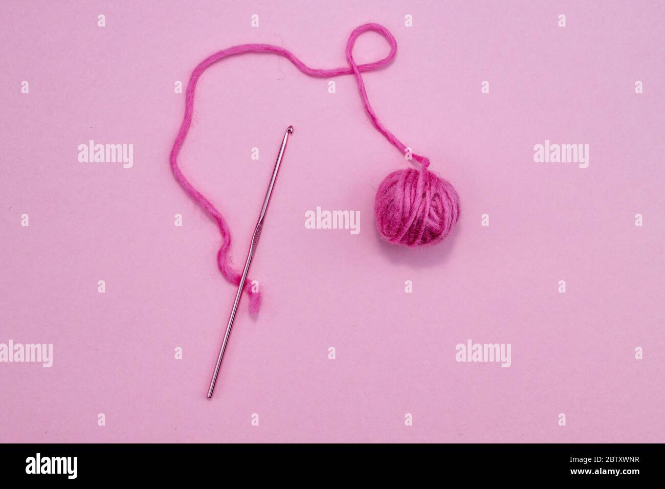 Gancho de ganchillo con bola rosa de lana sobre fondo rosa Foto de stock