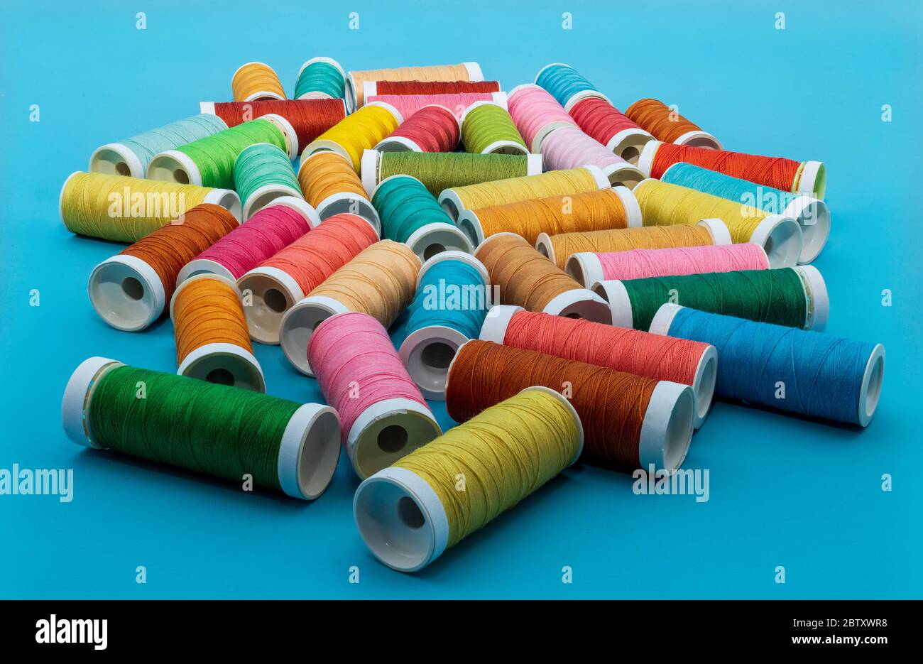 Carretes de hilo de coser en muchos colores sobre un fondo azul. Foto de stock