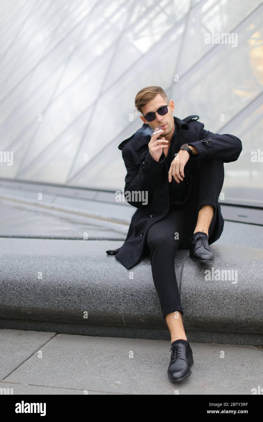 Joven hombre vestido chaqueta negra sentado en la Pirámide del Louvre y  fumando Fotografía de stock - Alamy