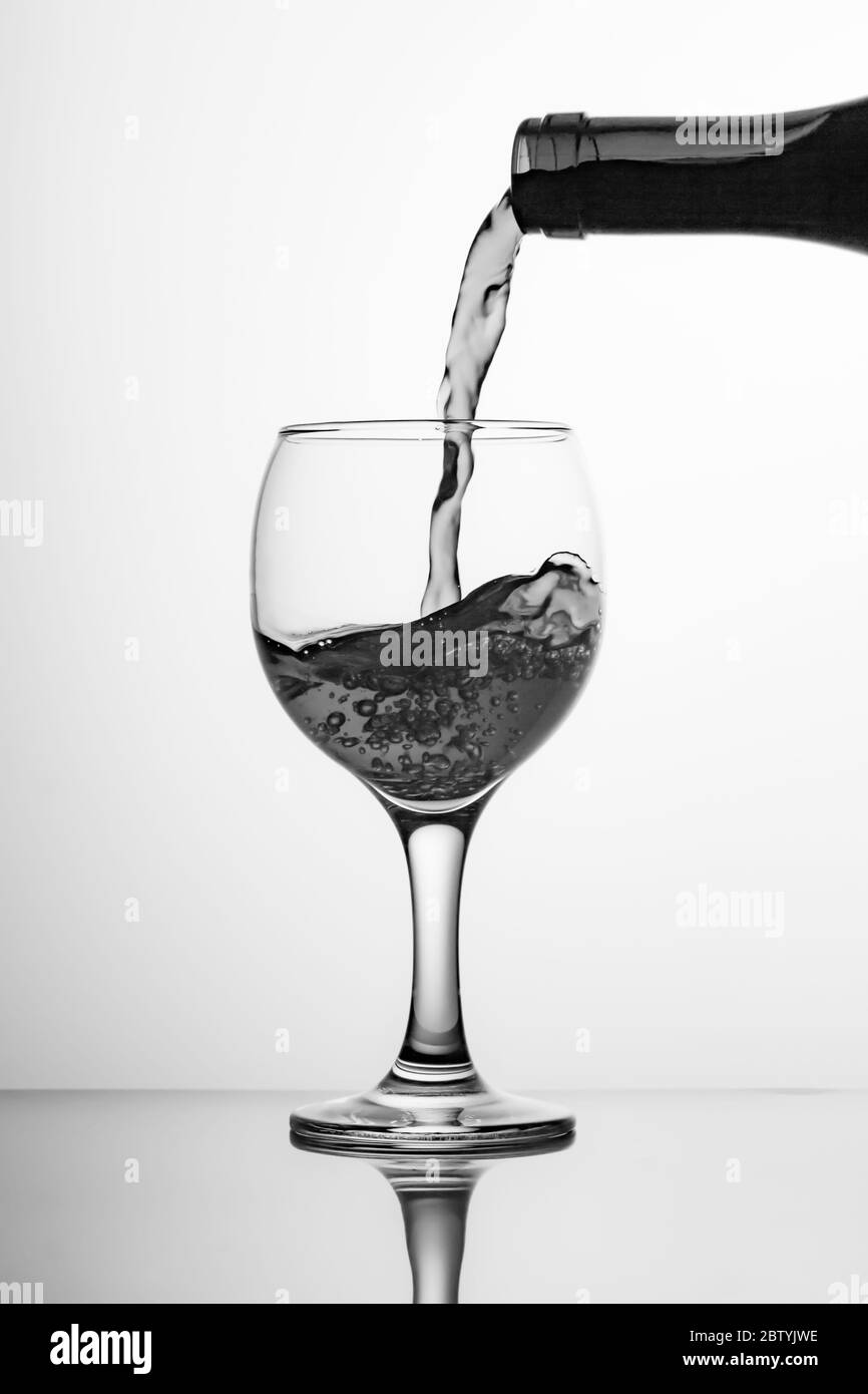 Imagen en blanco y negro de una botella de vino y una copa. Verter vino