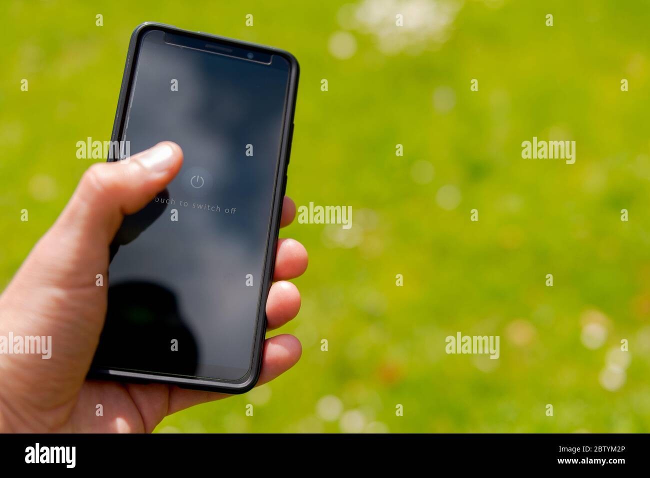 Mano humana sosteniendo el smartphone a punto de apagar el dispositivo con fondo borroso de jardín prado lucha digital fatiga Foto de stock
