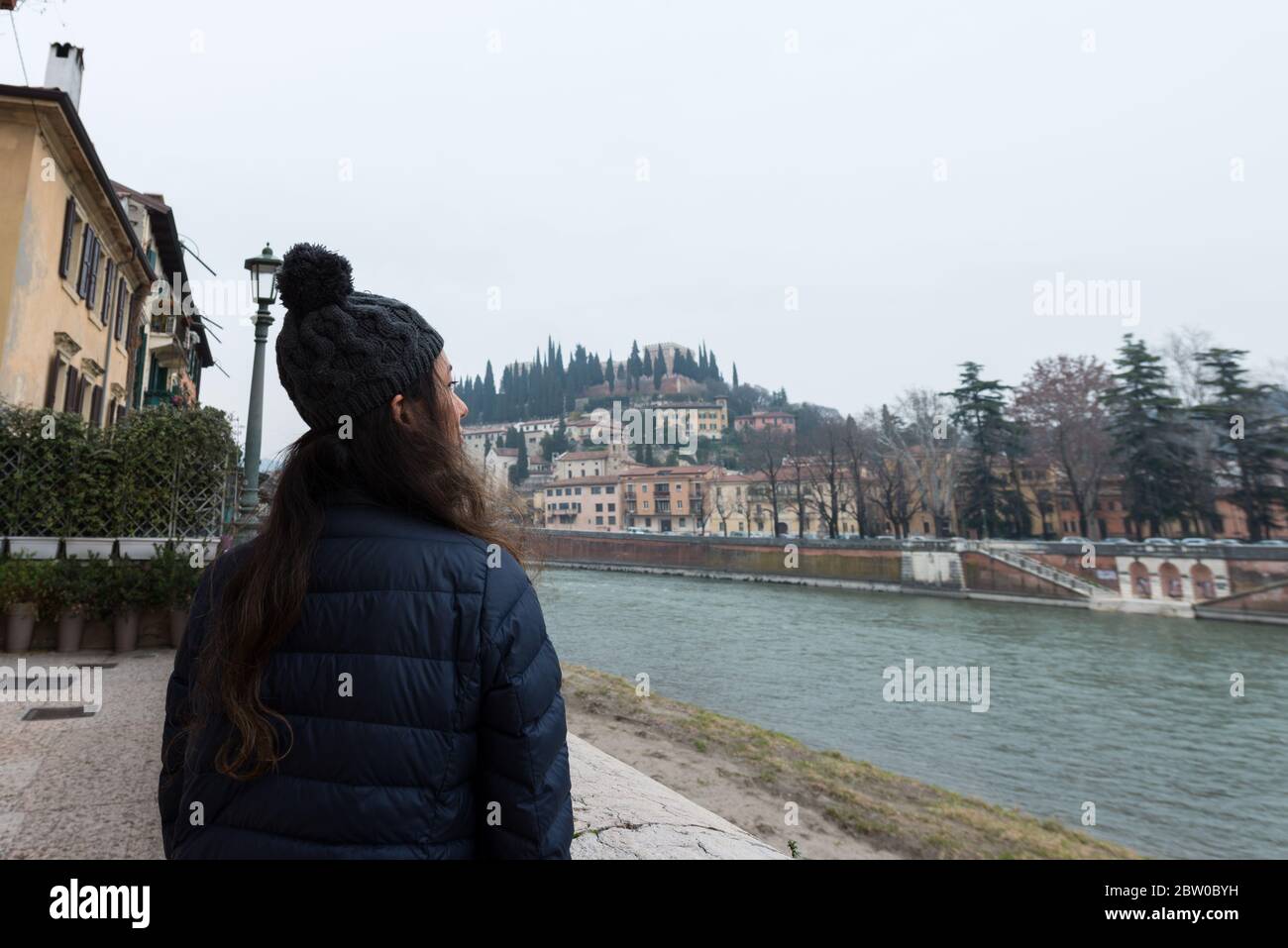 Imagen horizontal de una mujer morena mirando al horizonte de Verona durante un día frío, Italia Foto de stock