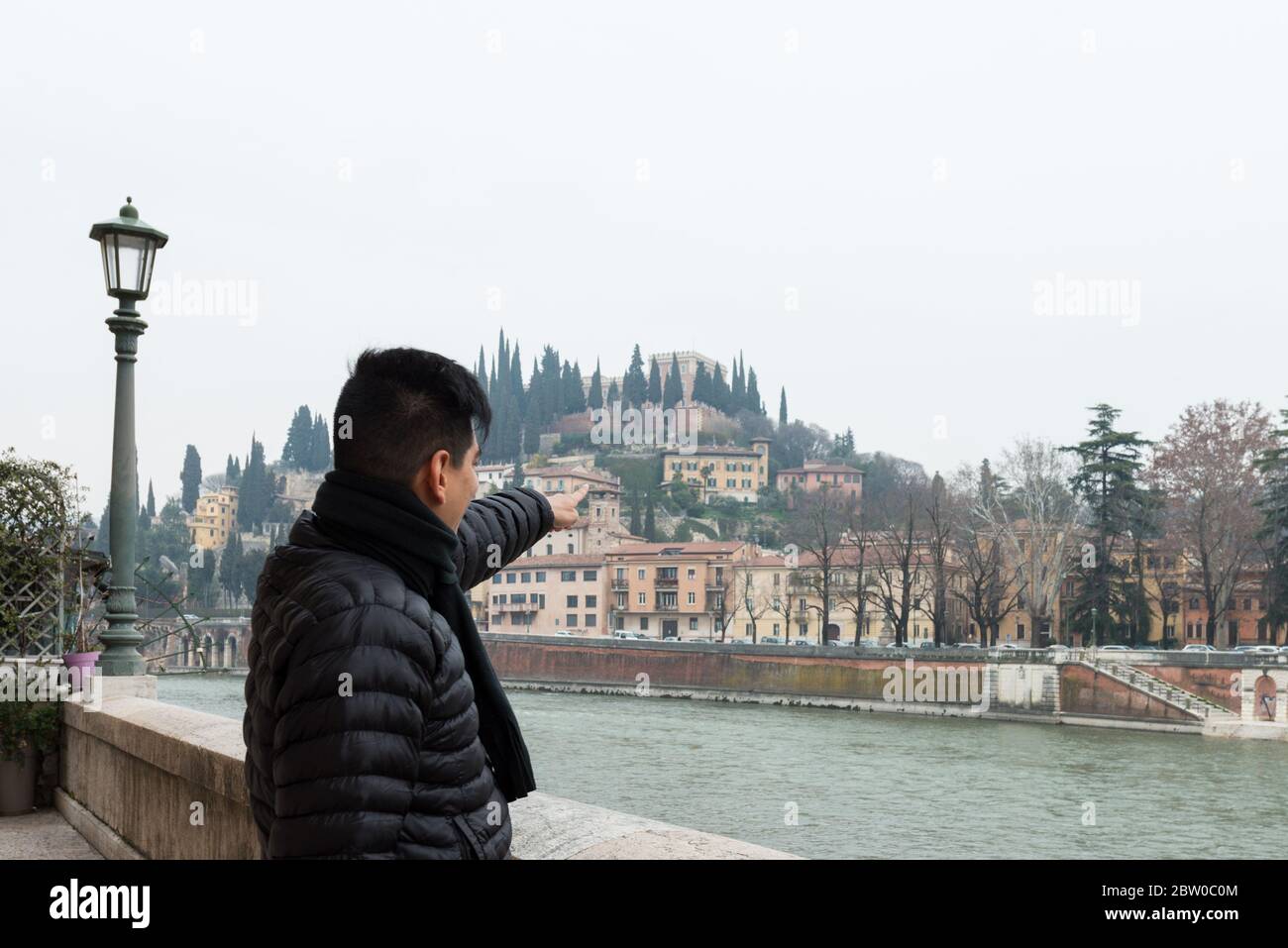 Imagen horizontal de joven apuntando al horizonte de Verona durante un día frío, Italia Foto de stock