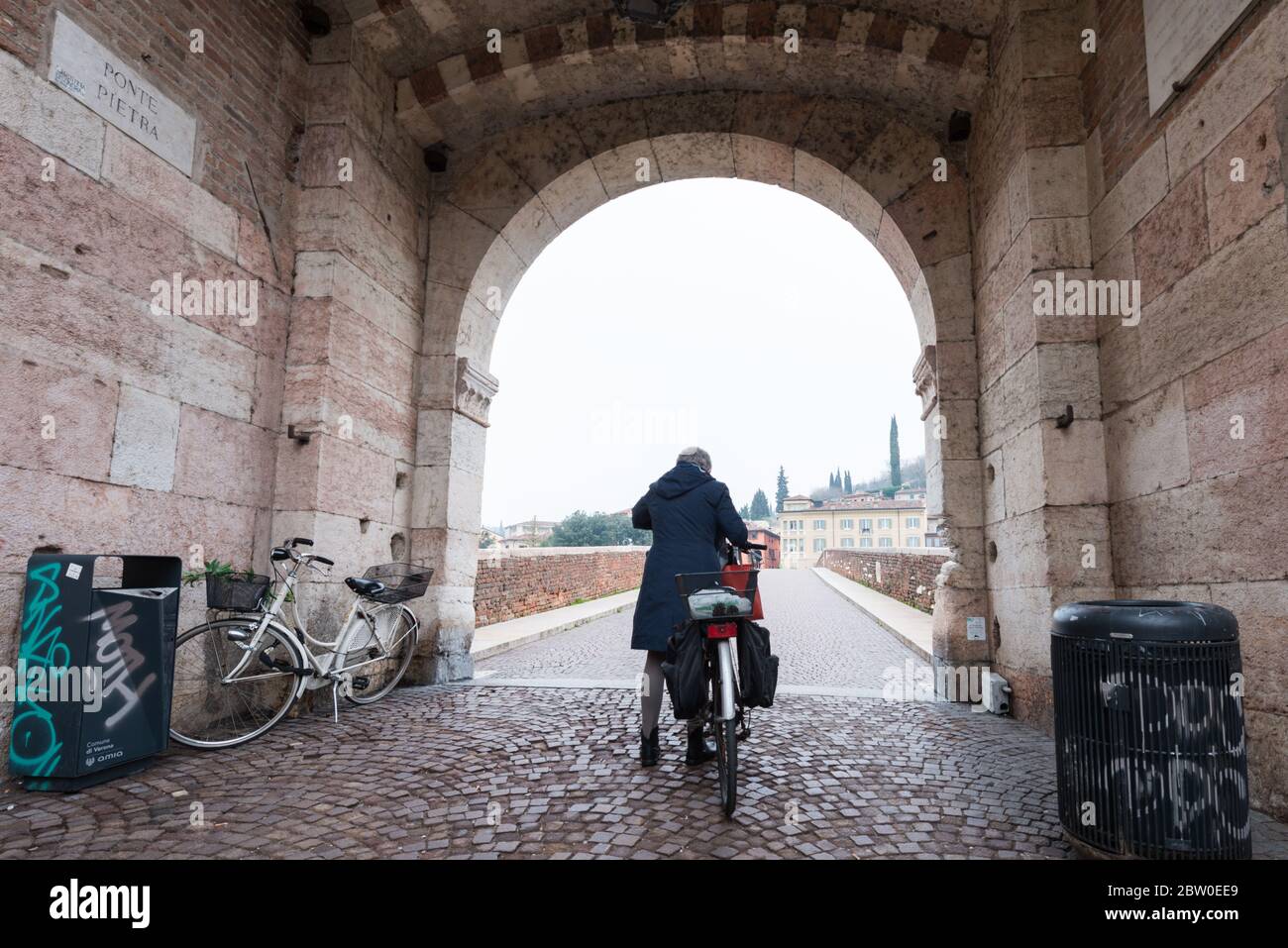 VERONA, ITALIA - 14, MARZO, 2018: Imagen de gran angular de la mujer con bicicleta en Ponte Pietra, un famoso puente de Verona, Italia Foto de stock
