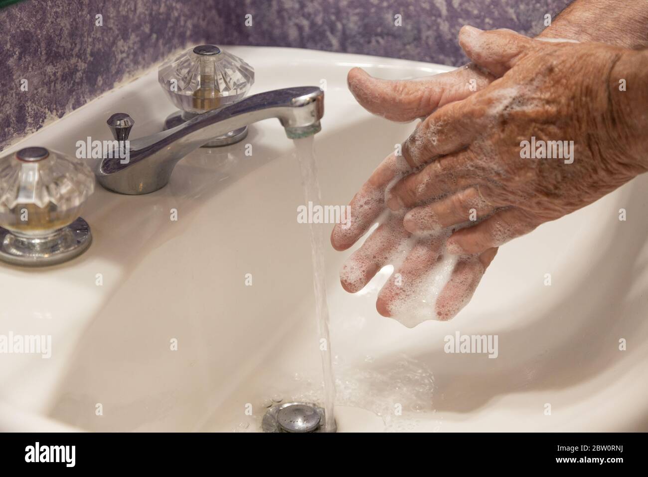 Hombre lavando las manos jabonosas en el lavabo del baño con agua corriendo por el desagüe Foto de stock