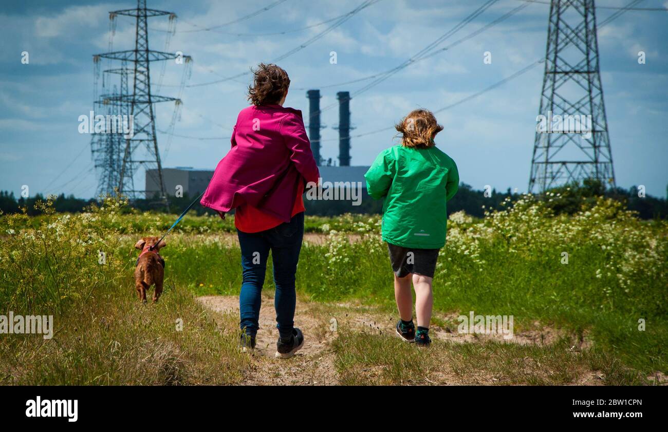 Una unidad familiar de madre e hija caminando a un perro en el campo cerca de la central eléctrica de Spalding a finales de la primavera en un día ventoso Foto de stock