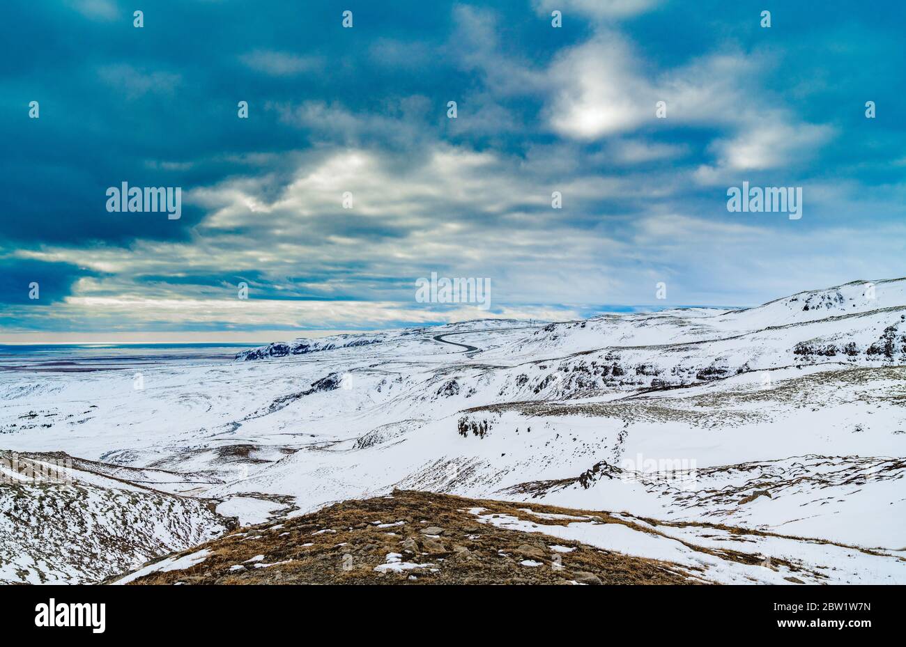 Nubes dramáticas sobre el paisaje de montaña cubierto de nieve con camino adentro el fondo Foto de stock