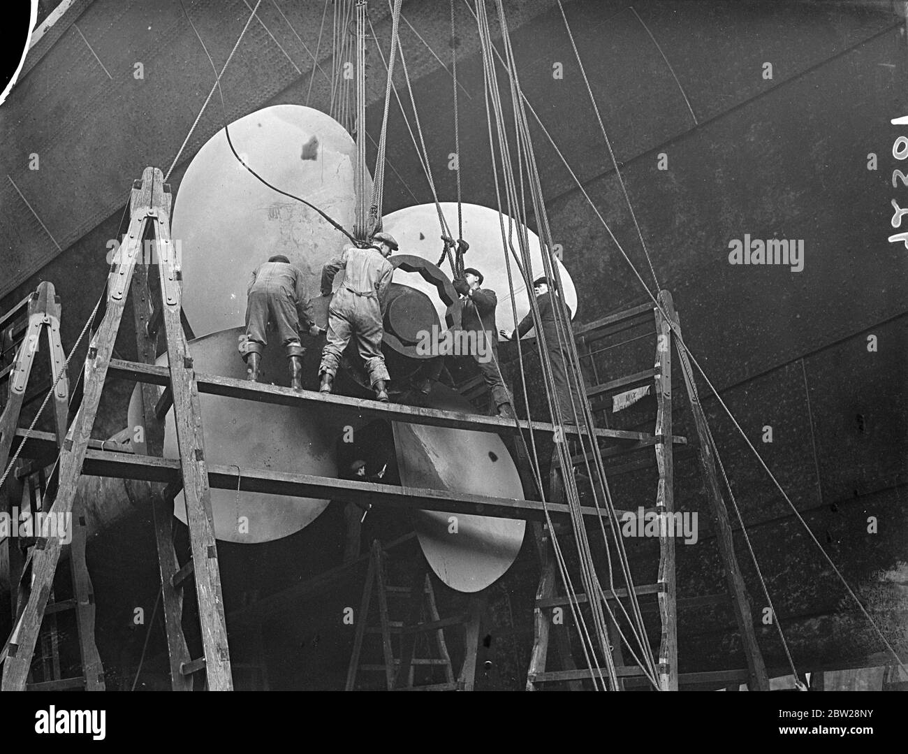 'RMS Queen Mary' revisado en muelle seco. Un pequeño ejército de hombres se dedica ahora a la limpieza del casco submarino de la gigante de 80,000 toneladas de línea 'Reina María' que ahora está en el muelle seco Rey Jorge V en Southampton para la revisión. Muestra de fotos, los hombres trabajan en uno de los hélices gigantes. 30 de diciembre de 1937 Foto de stock