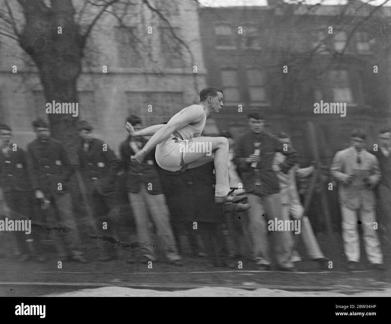 Gran encuentro atlético triangular en Westminster. E Cawston en un salto largo en el gran concurso atlético triangular entre Westminster , Eastbourne College y Achilles Club en el terreno de Vincent Square , Londres . 4 de abril de 1932 Foto de stock