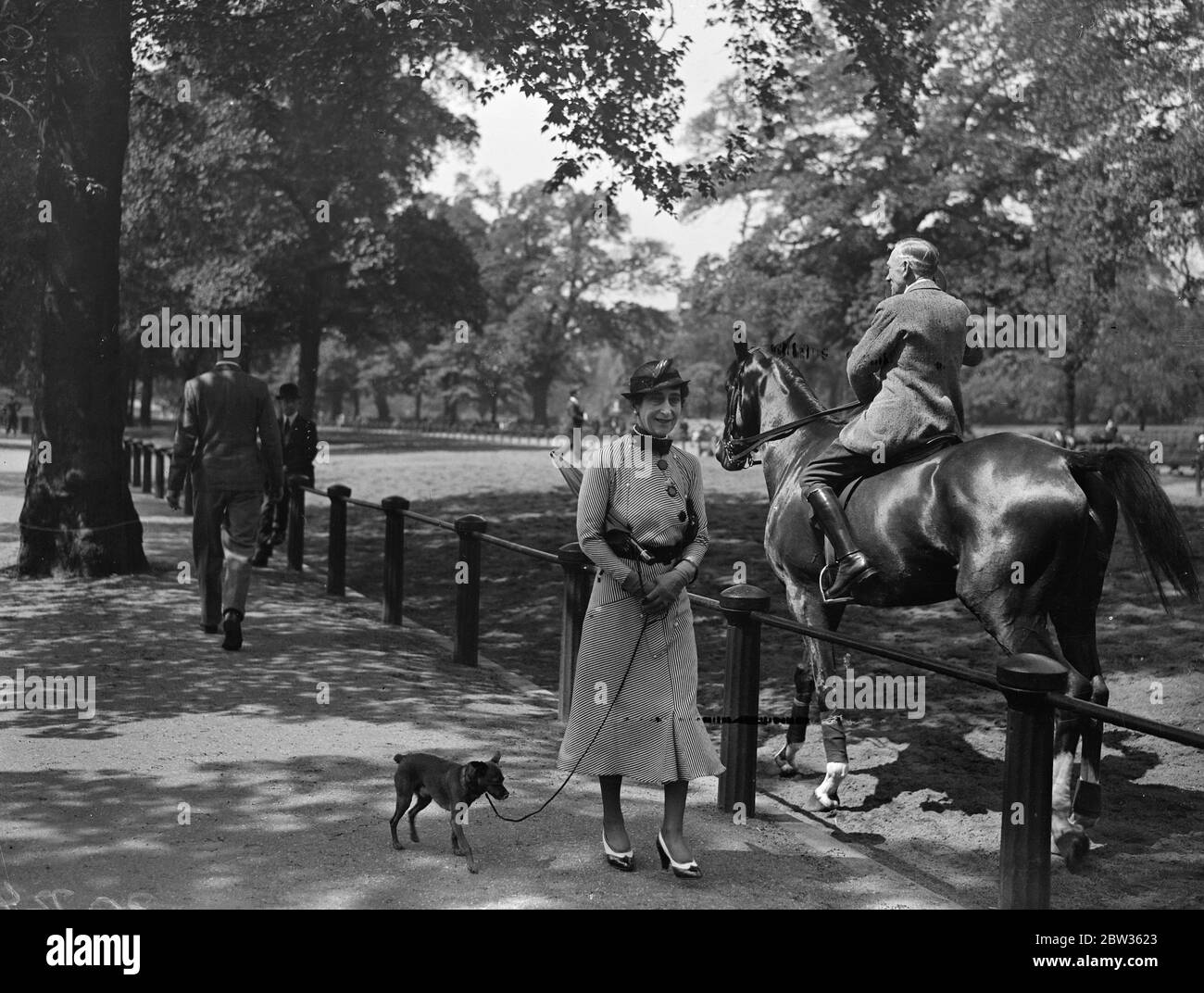 Reina de Noruega en el Parque . El Qeen de Noruega aprovechó la hermosa luz del sol para dar un paseo por Hyde Park y ver a los jinetes en Rotten Row. La Reina Maud de Noruega acompañado por su perro mascota viendo a los jinetes en la fila en Hyde Park. 20 de mayo de 1933 Foto de stock