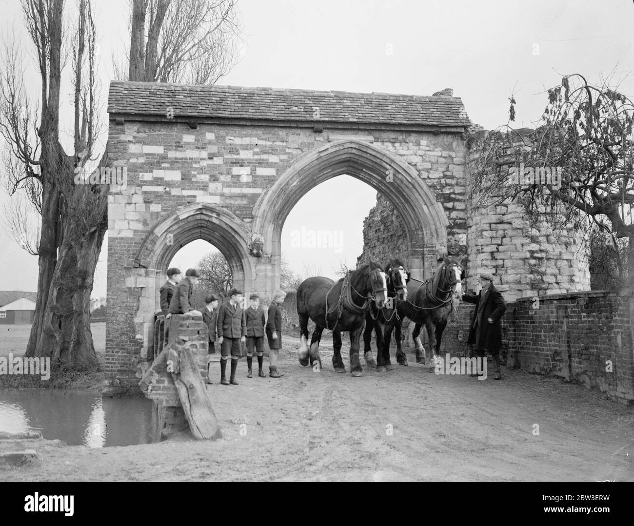 Remanente de un pasado glorioso. Un equipo de caballos de granja pasando bajo la puerta de entrada a la Abadía de Waltham , que tiene 875 años de edad. 15 de enero de 1935 Foto de stock