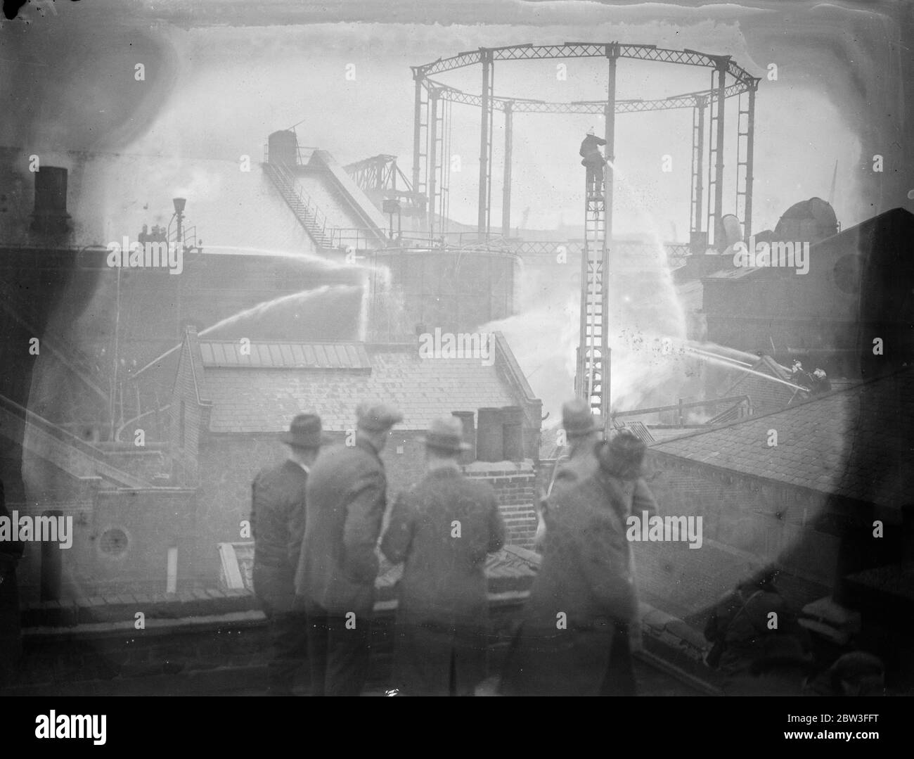 Hombres viendo bomberos trabajando tratando con las grandes obras de gas en Wapping , Londres . 26 de enero de 1935 Foto de stock