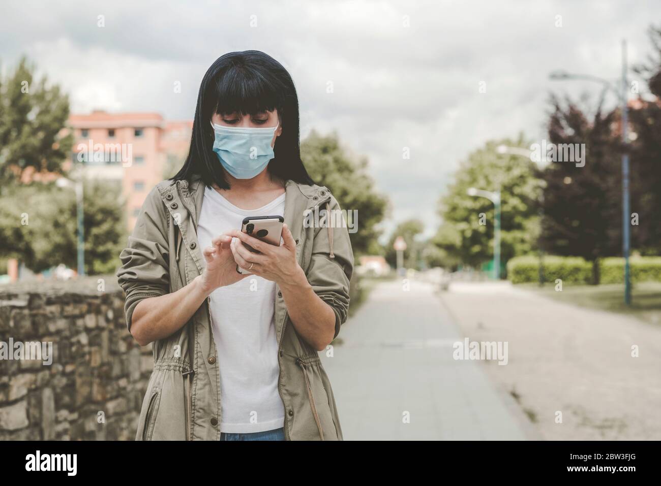 Mujer con máscara médica con su smartphone en la calle al aire libre Foto de stock