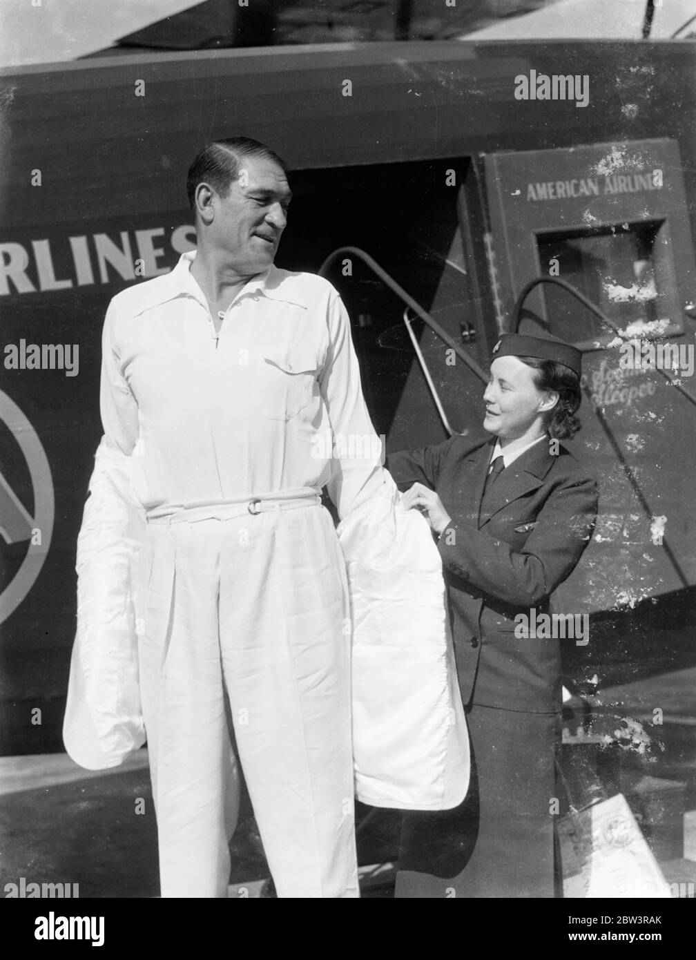 ¡el abrigo más viajado del mundo! . Hecho para Victor McLaglen en Londres, el buque aéreo Hindenburg lo llevó a través del Atlántico. En cuatro días de haber puesto el último puntadas en un abrigo deportivo adaptado en Londres, Victor McLaglen , el actor de cine, llevaba el abrigo en los Ángeles . El abrigo fue volado desde Londres a Friedrichshafen , Alemania , por aviones de línea y luego fue llevado a Lakehurst , Nueva Jersey , en el Airship Hindenburg . Desde allí fue volado a los Ángeles por American Airlines. Espectáculos de fotos, Victor McLaglen intentando en el abrigo con la ayuda de la mayordomo Mae Byrne después de su llegada Foto de stock