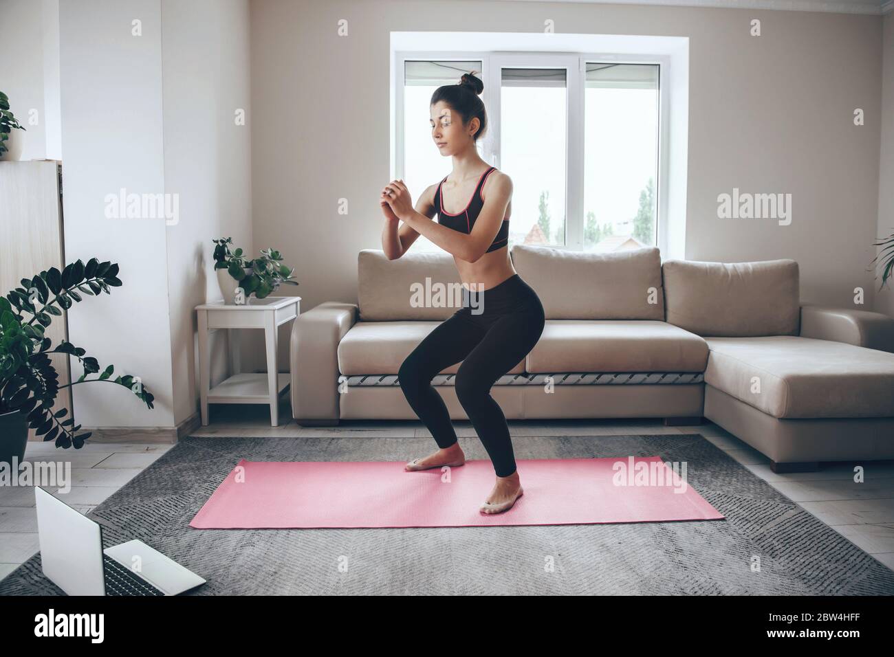 Mujer morena en forma en leggins blancos y top haciendo yoga en la alfombra  en casa