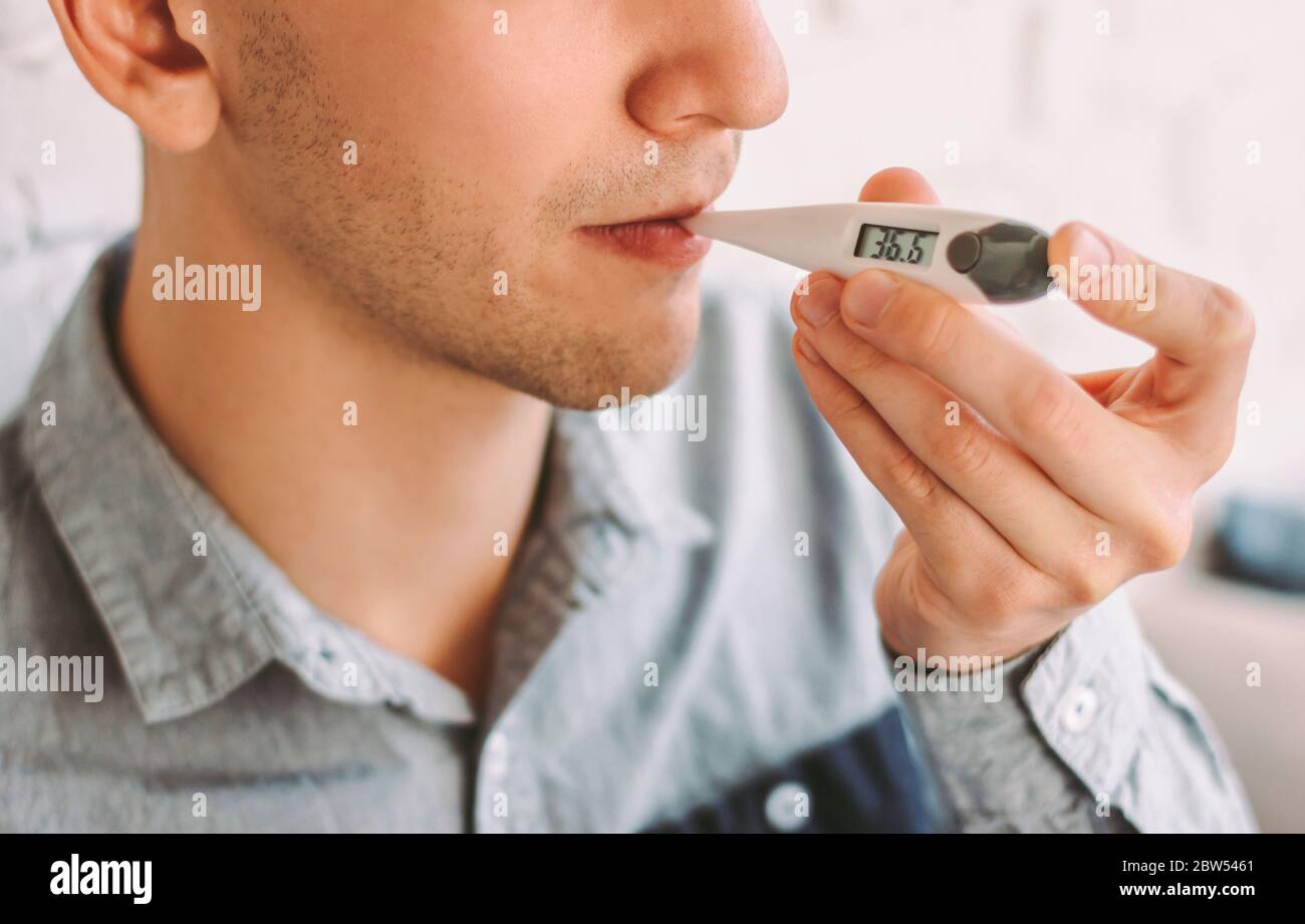 Closeup hipster hombre freelancer sosteniendo termómetro digital en la boca  para medir la temperatura corporal en casa. Estudiante de negocios enfermo  cheque tempera Fotografía de stock - Alamy