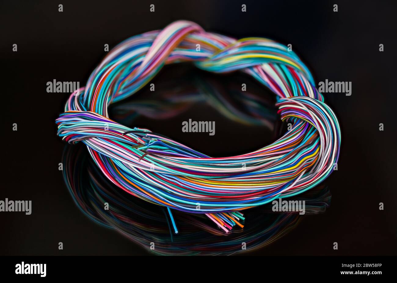 Mazo de cables eléctrico de cables de colores enredados. Cableado multifilar trenzado redondo de conductores de cobre aislados. Reflexión sobre fondo negro Foto de stock
