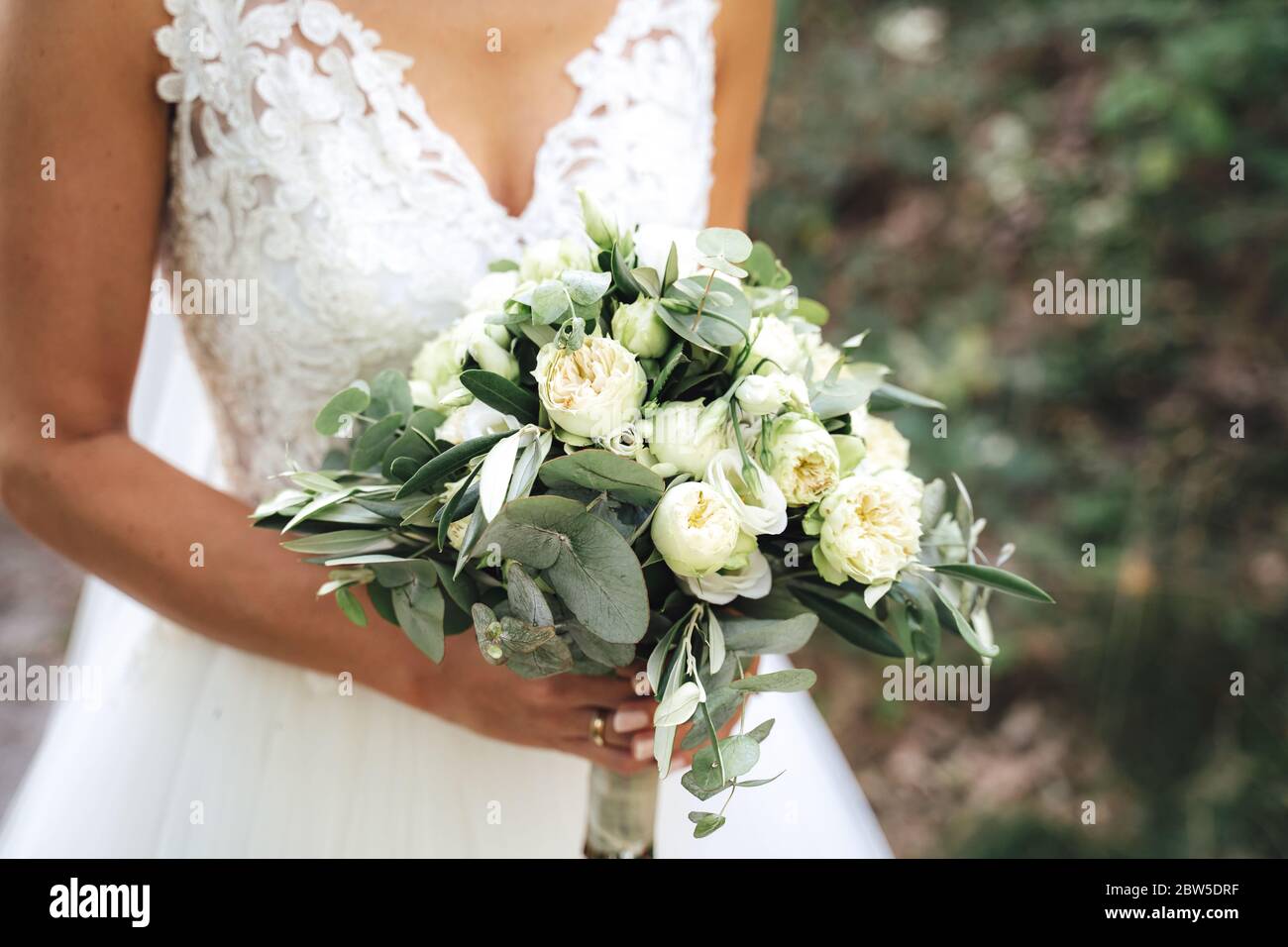 Novia sosteniendo un ramo de boda blanco / verde en sus manos contra una  bata blanca. Concepto de día de boda Fotografía de stock - Alamy
