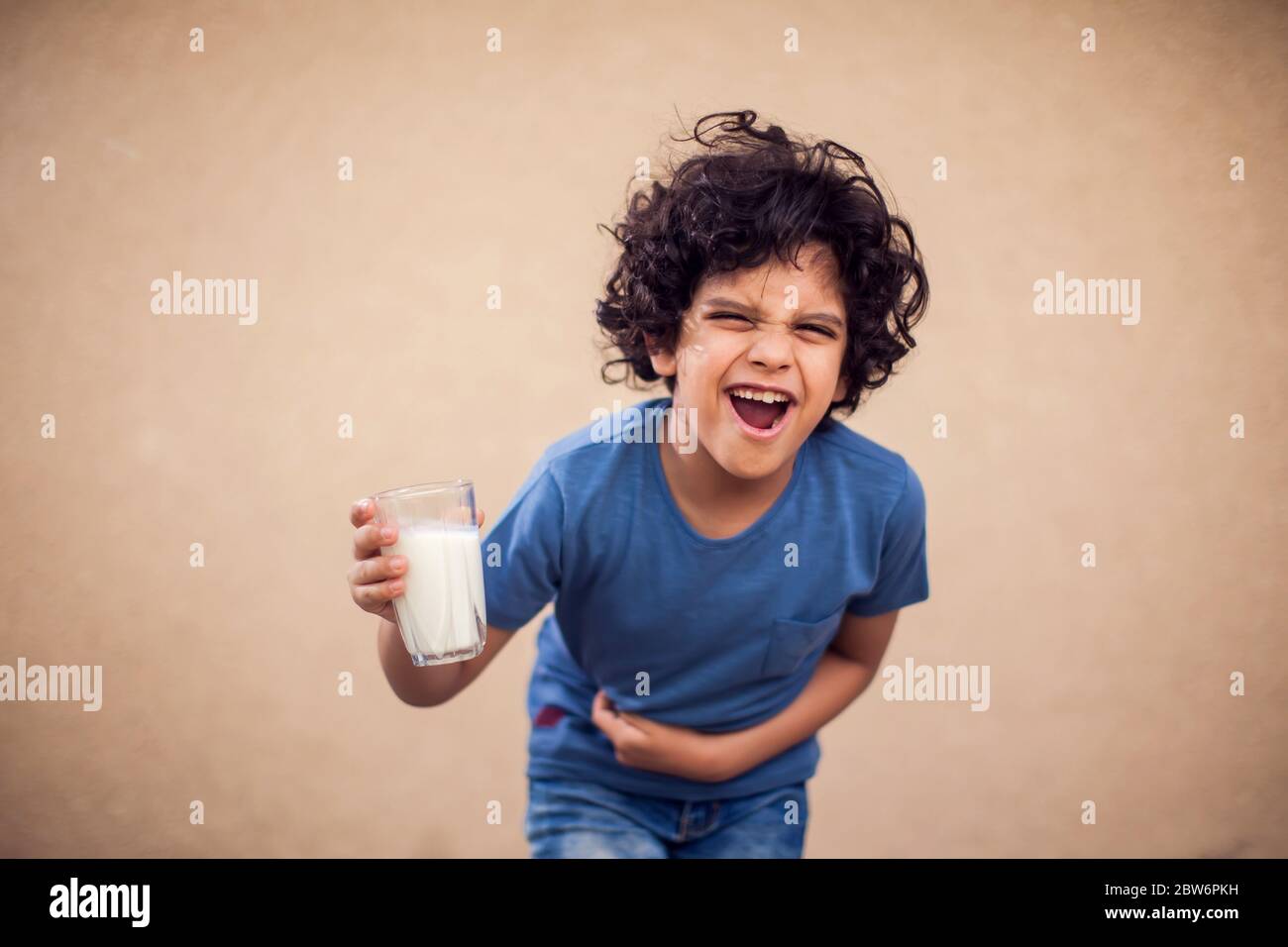 Un niño sostiene un vaso de leche y siente dolor de estómago fuerte. Niños, cuidado de la salud y concepto de alimentos Foto de stock