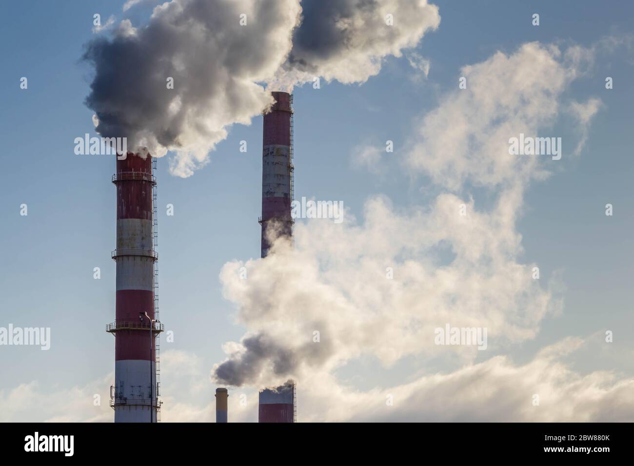 Tuberías de fábrica con humo sobre fondo azul cielo. Chimeneas industriales que envían humo grueso al cielo azul. Contaminación del aire. Problema ecológico mundial. Foto de stock