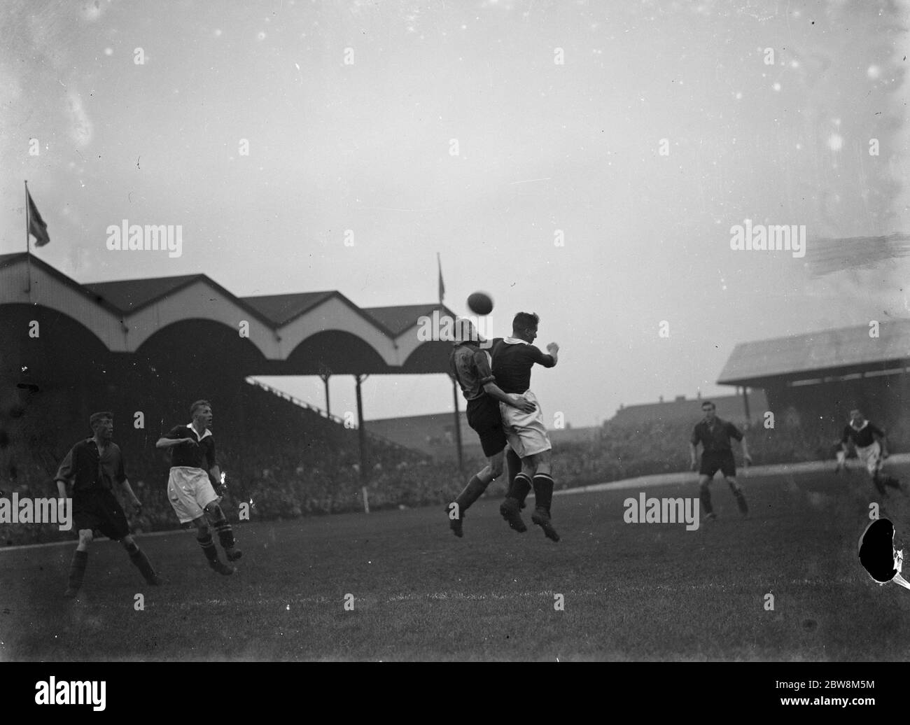 Partido de fútbol; dos jugadores compiten por el fútbol en el aire. 1935 Foto de stock