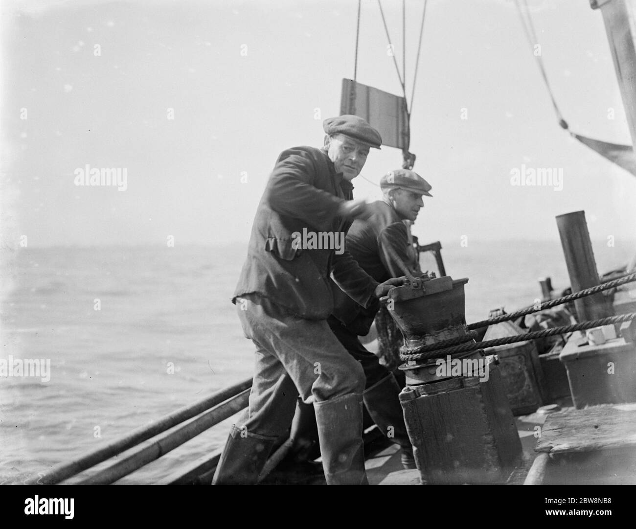 Un crewman en un barco de camarones trabaja el cabrestante de la cuerda del brazo. 1936 Foto de stock