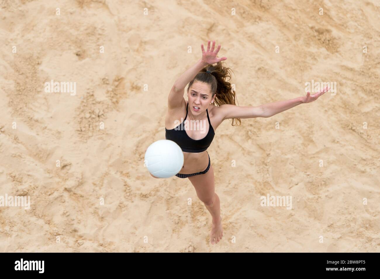 Mujer joven con pelota blanca jugando voleibol en la playa. Vacaciones de verano y concepto deportivo Foto de stock