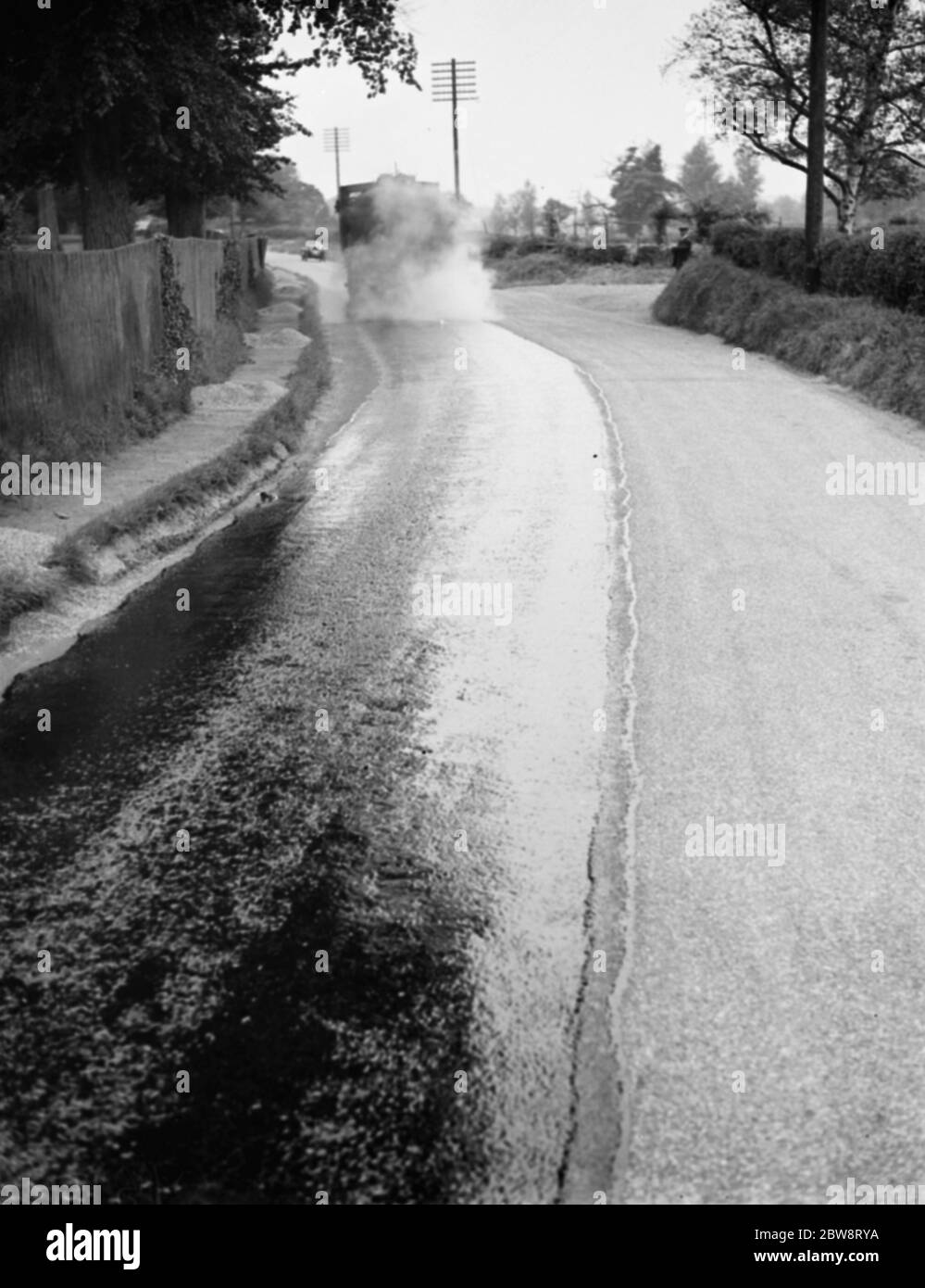 La carretera está siendo pavimentada por una máquina de pulverización de alquitrán de Taroads Limited. 1938 Foto de stock