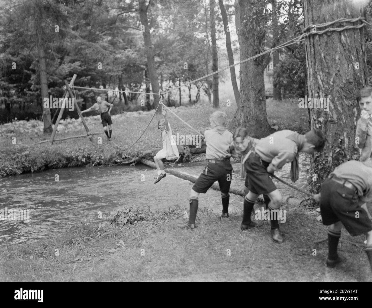 Scouts usando una silla de un jovencito para tirar de dos niñas pequeñas a través de un arroyo. 19 de junio de 1939 Foto de stock