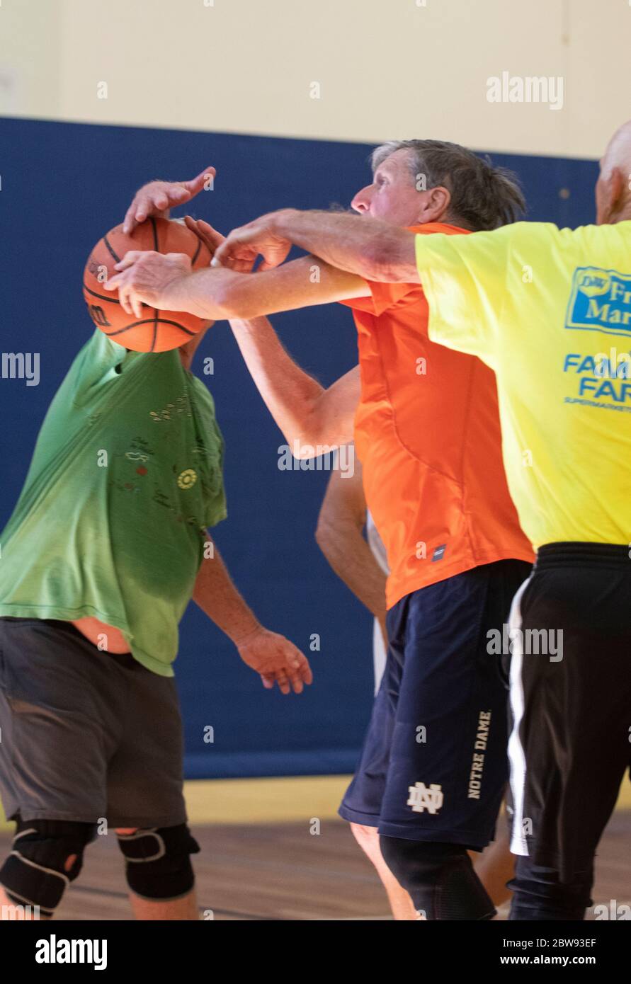 Un jugador de baloncesto senior interbloquea los brazos con otros jugadores un centro de recreación en Englewood, Florida, EE.UU. Foto de stock