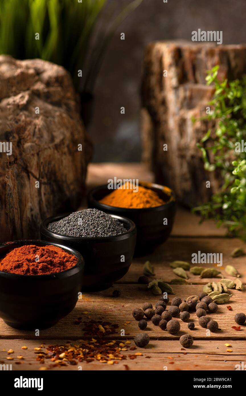 Tres pequeños cuencos negros con curry, semillas de amapola y paprika dulce sobre una mesa de madera Foto de stock