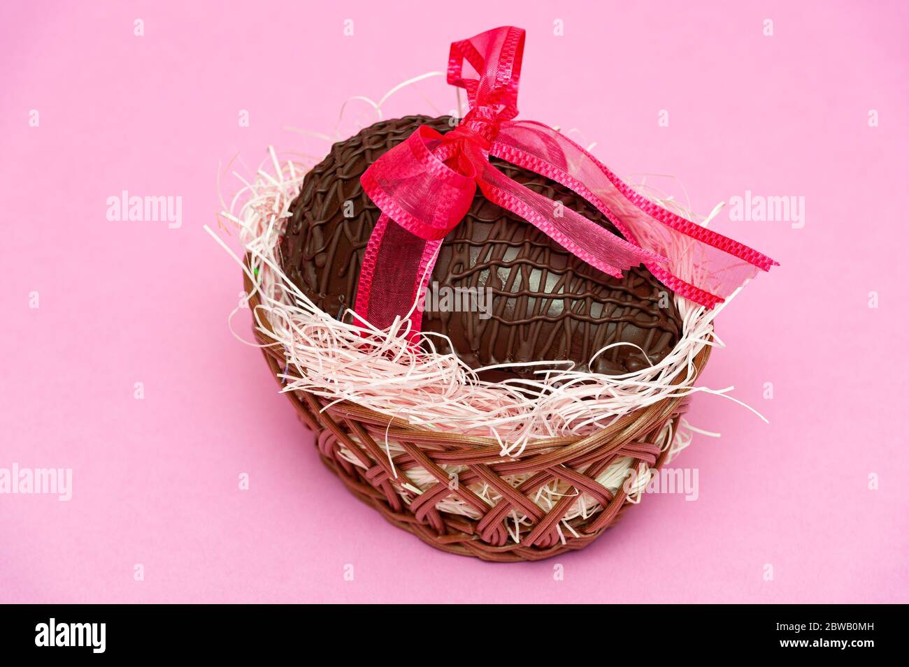 Huevo de chocolate en una hermosa cesta de mimbre con cinta roja para  regalo. Celebración del día de la Madre, día de San Valentín y Pascua.  Aislado en el backgroun rosa Fotografía