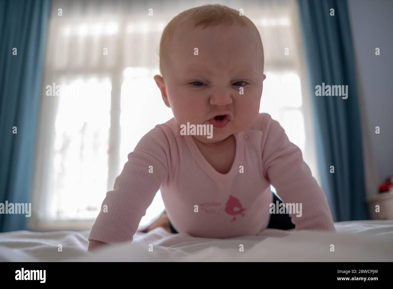 Lindo bebé niña de pie en la cama hacer caras divertidas, cara enojada, llorando por la mañana Foto de stock