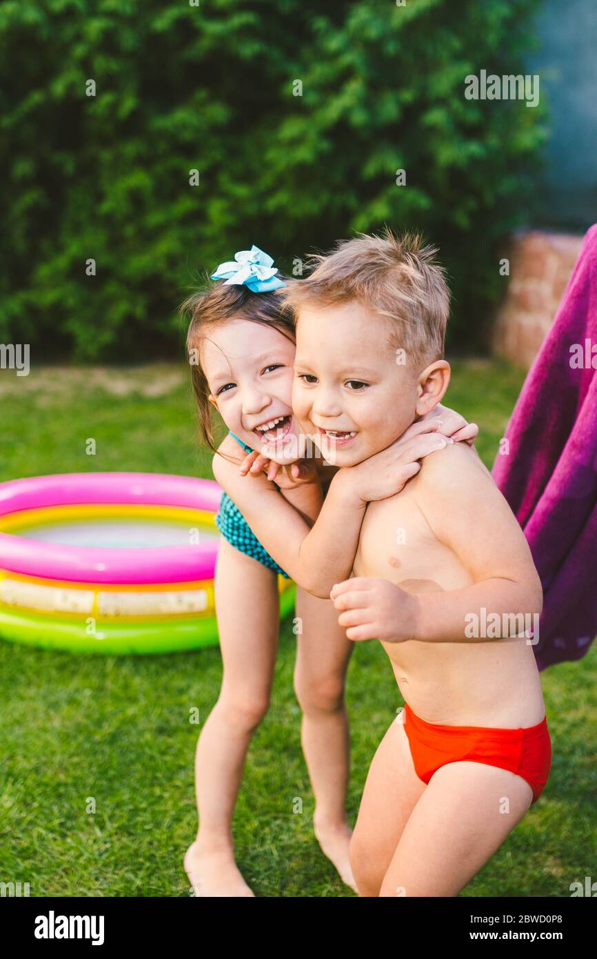 Los niños caucásicos felices juegan, envueltos en una toalla de playa grande de verano en el calor después de nadar en una piscina inflable casa redonda Foto de stock