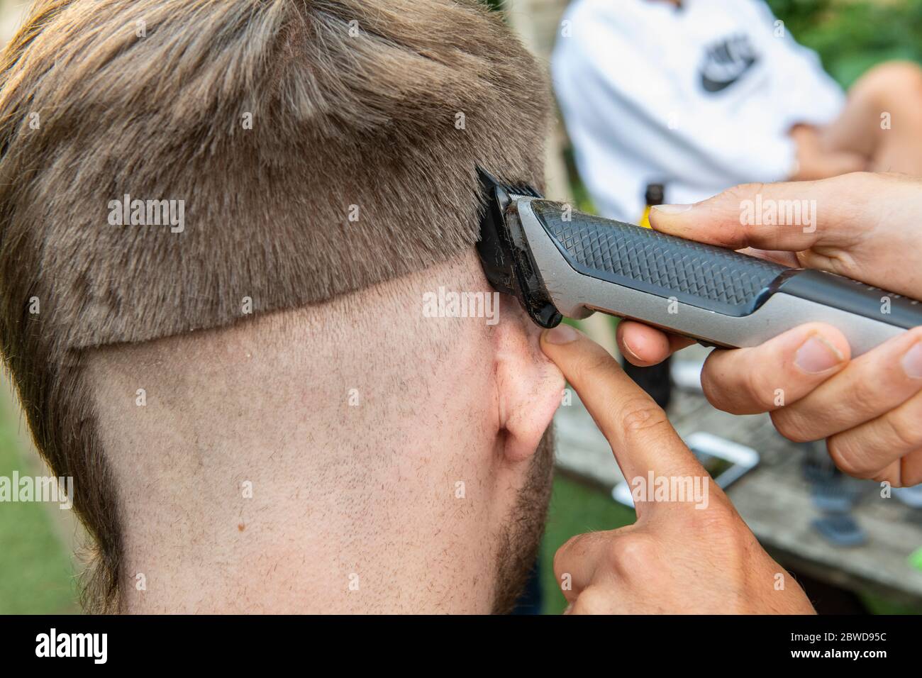 Un hombre intenta cortar el pelo de otro hombre durante el cierre del coronavirus cuando los peluqueros están cerrados, dejando la cola de una rata abajo un lado de la cabeza Foto de stock