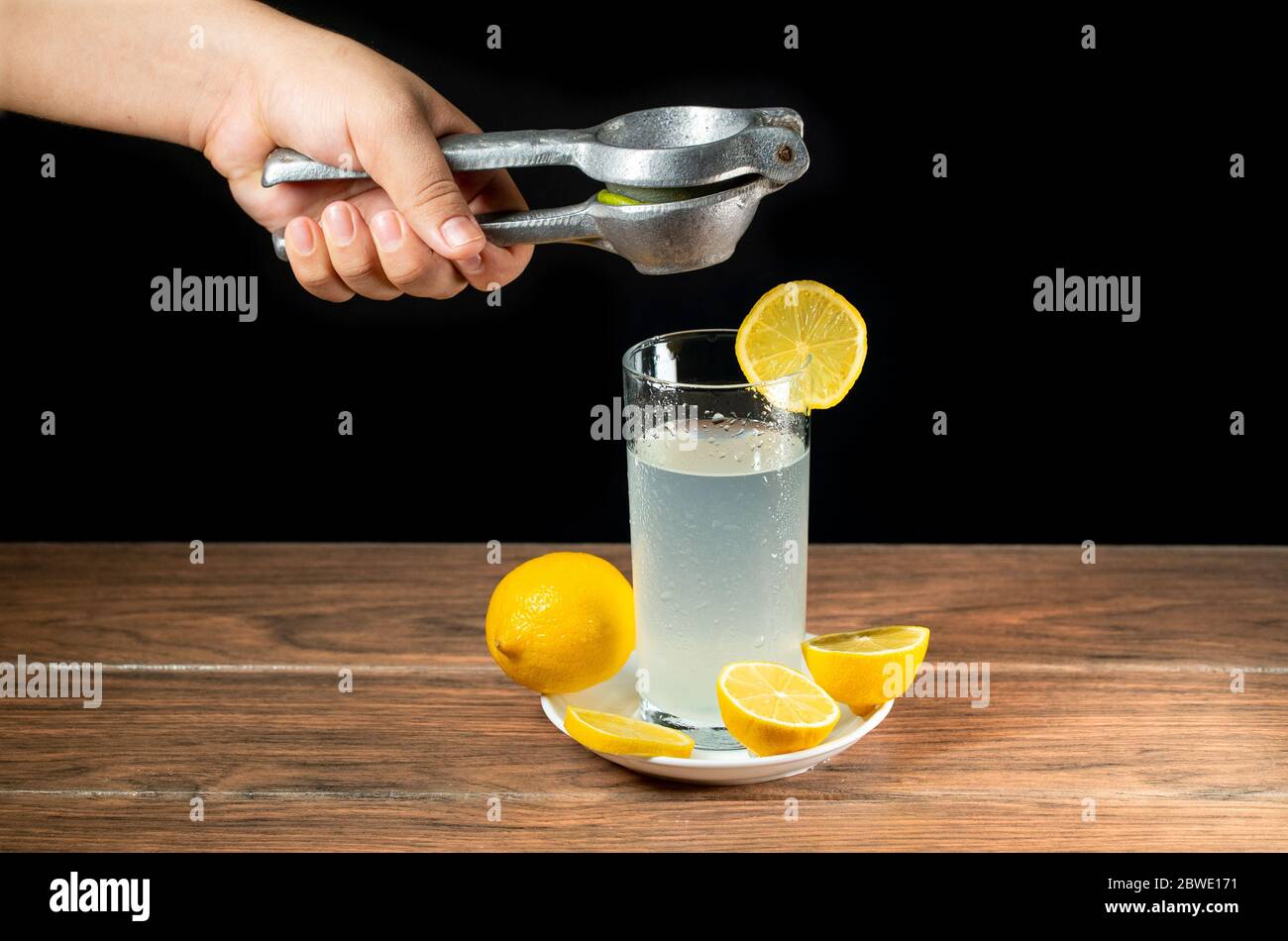 Exprimir un limón en un cristal de limonada con limones amarillos alrededor  de un plato blanco, haciendo una limonada comida oscura Fotografía de stock  - Alamy
