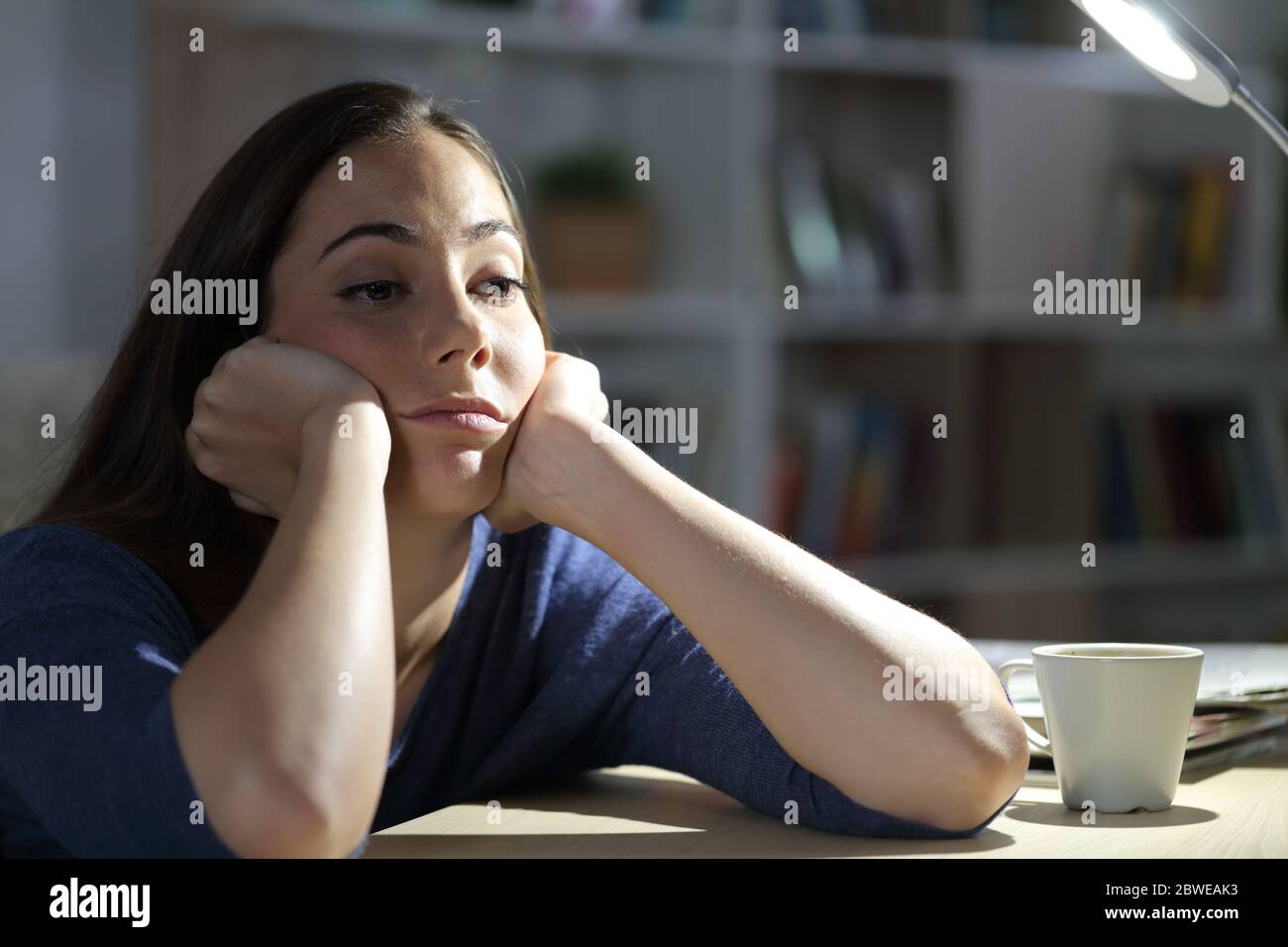 Mujer aburrida mirando fuera de la hora de la cintura en la noche sentada en la sala de estar en casa Foto de stock