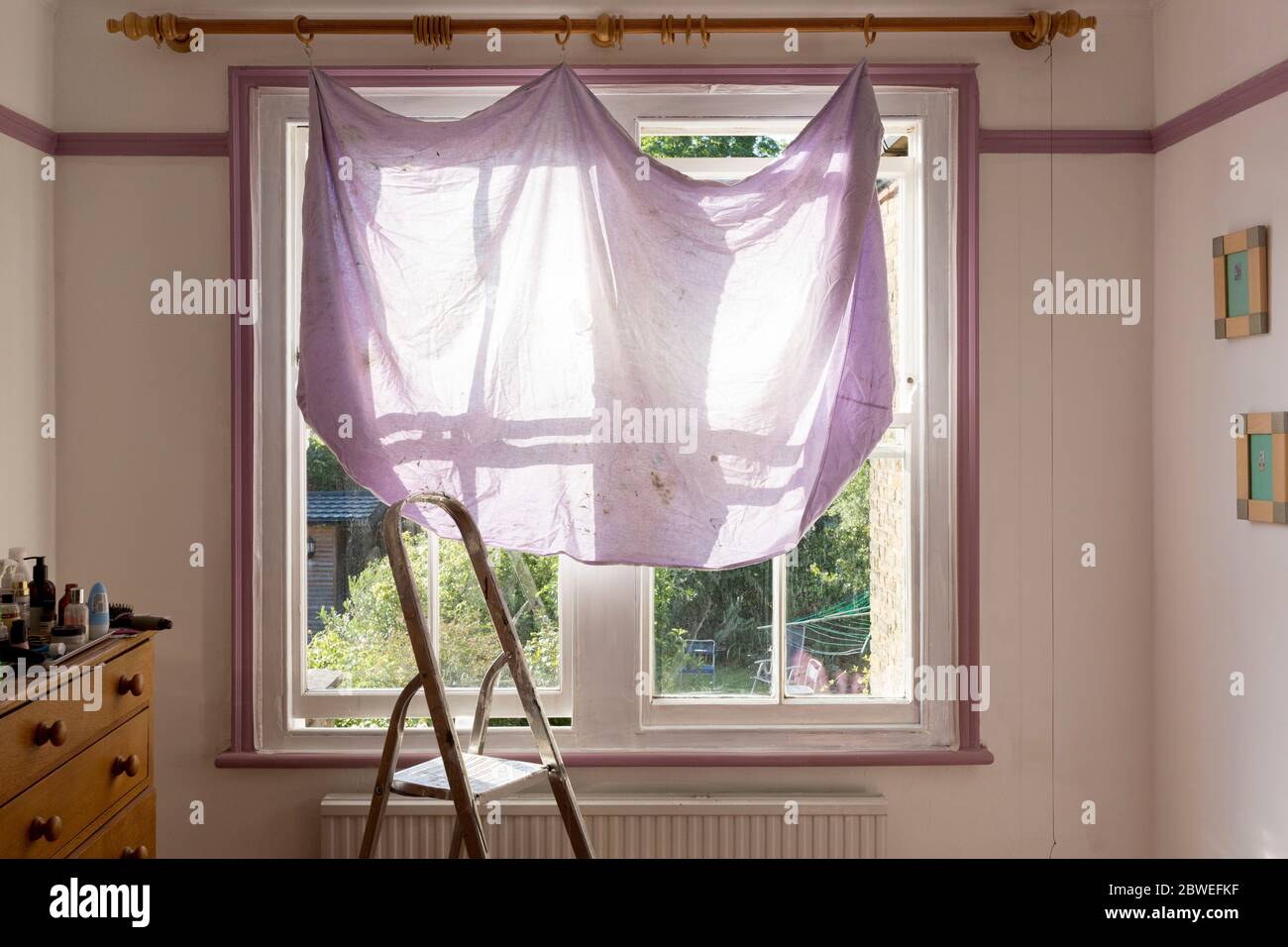 Una cortina temporal que sombrea la luz del sol de la mañana fuerte, cuelga de un carril a través de una ventana de dormitorio durante las reparaciones de la casa y la pintura de una ventana de la guillotina en una casa del período en el sur de Londres, el 25 de mayo de 2020, en Londres, Inglaterra. Foto de stock