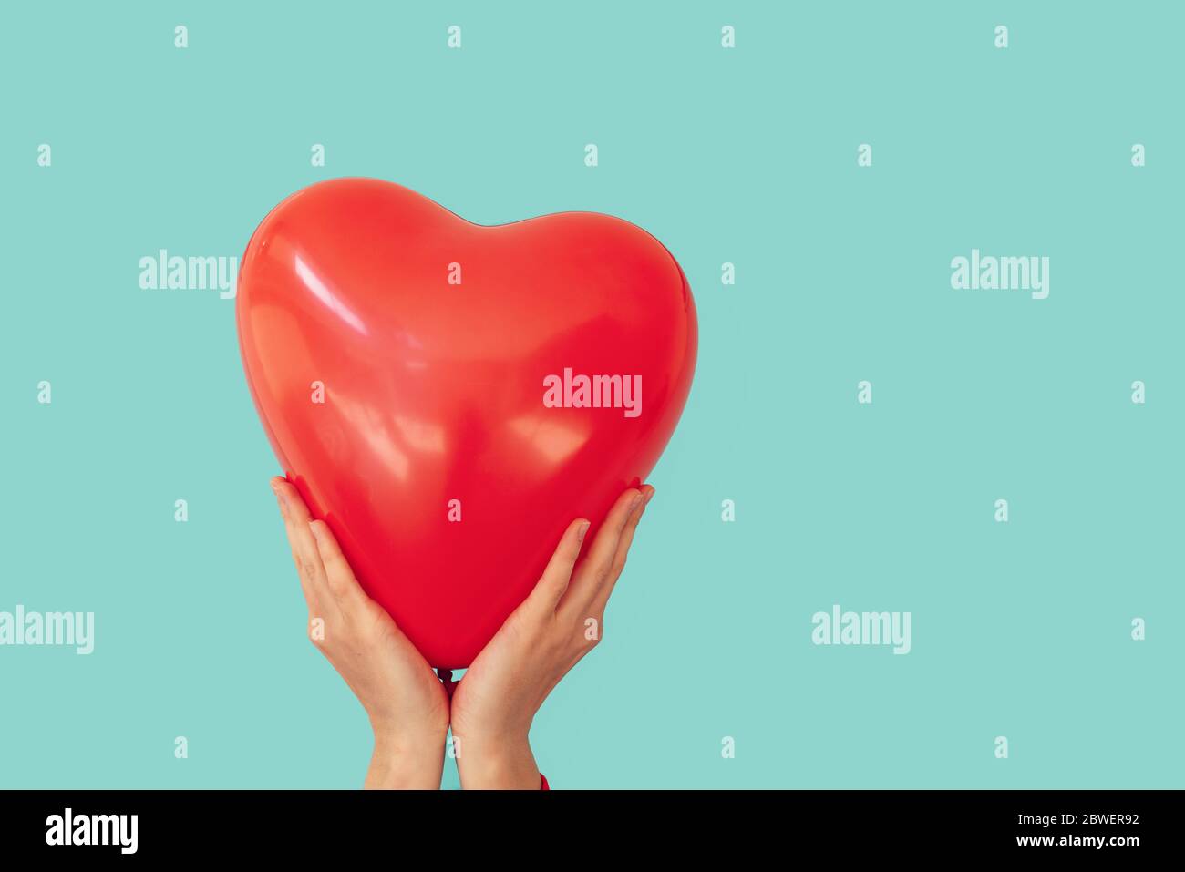 La mujer sostiene un globo rojo en forma de corazón sobre un fondo de pared turquesa. Día de San Valentín y concepto de romance Foto de stock
