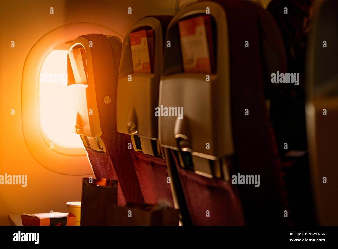 Vista posterior del asiento económico con folleto de papel en la caja sobre la mesa de plástico de la bandeja del avión. Luz del sol pasando por el avión de clase económica Foto de stock