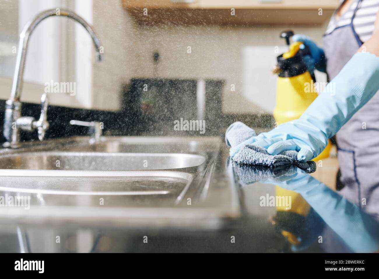 Imagen de cerca de la mujer rociando detergente desinfectante en el mostrador de la cocina y el fregadero para matar todas las bacterias Foto de stock