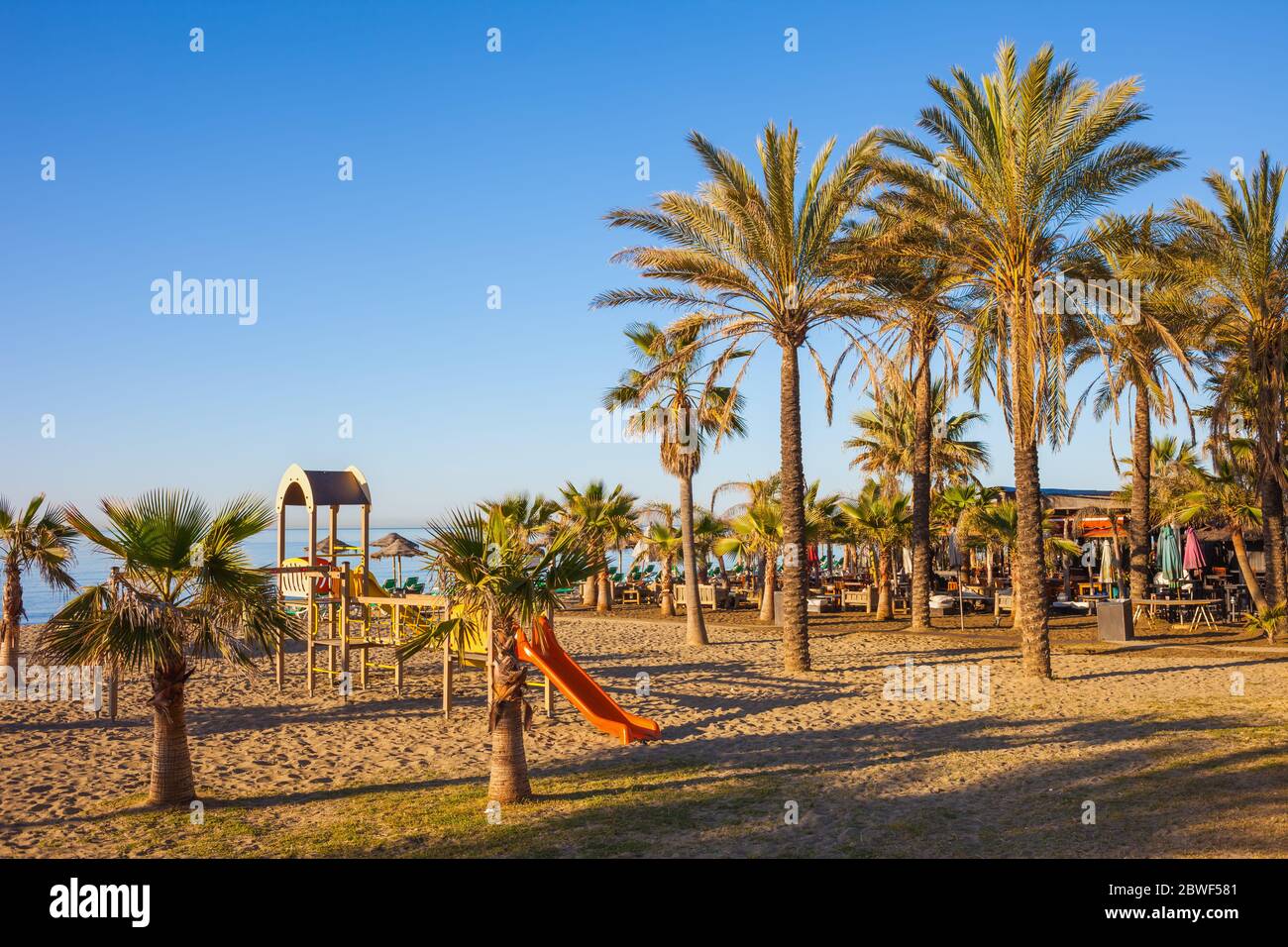 Playa en la Costa del Sol en Marbella, España, paisaje de vacaciones de verano con palmeras y parque infantil, temprano por la mañana Foto de stock