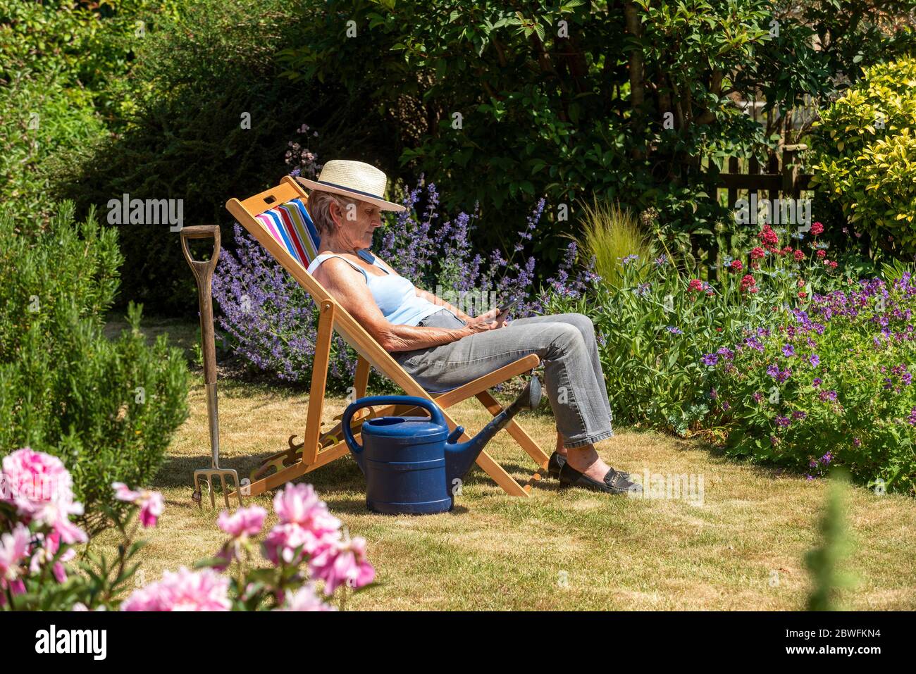 Hampshire, Inglaterra, Reino Unido. 2020. Mujer tomando un descanso de la jardinería sentado en una tumbona en un caluroso día de verano. Foto de stock